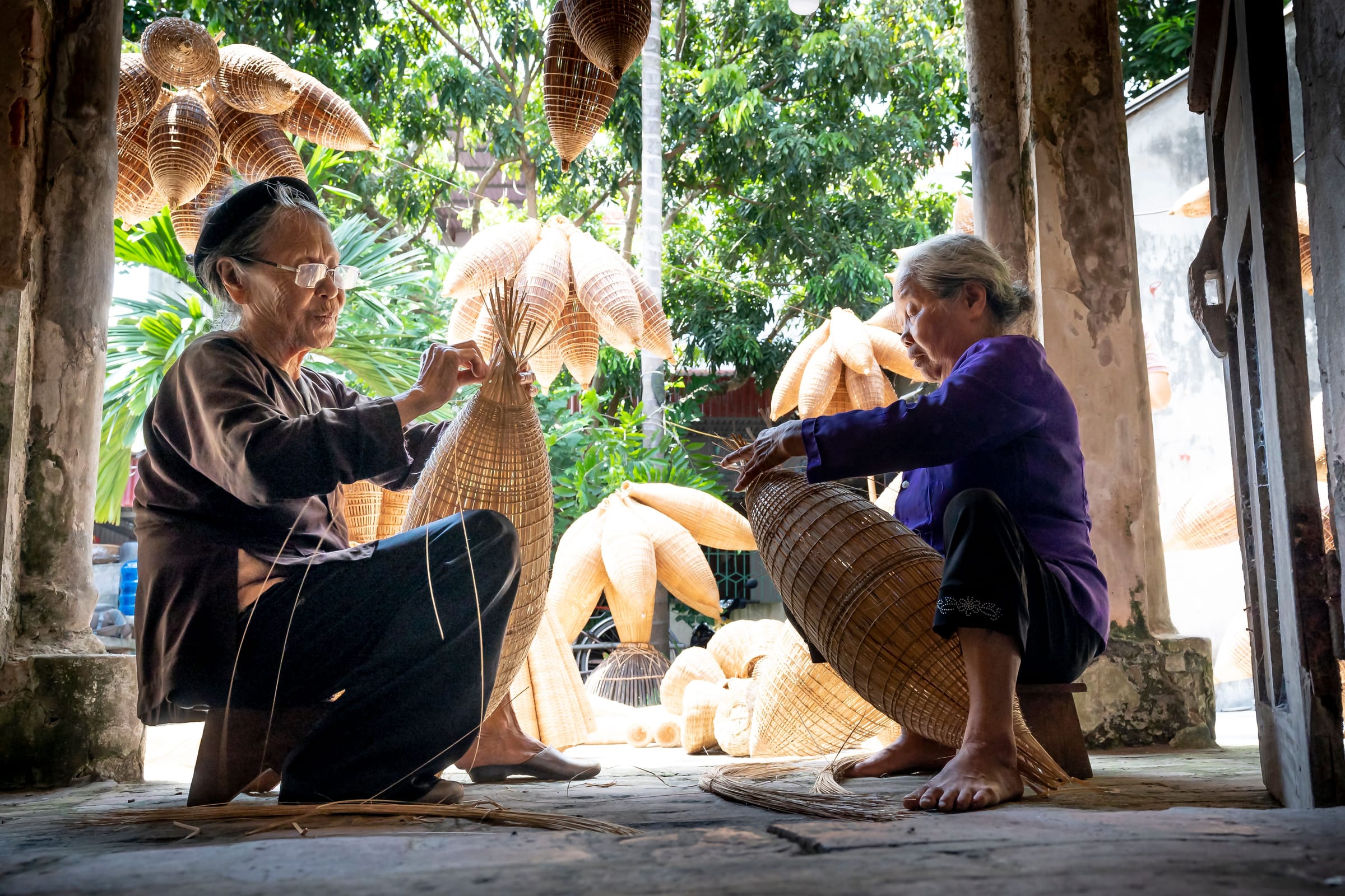 Two artisans weaving baskets by hand in a workshop, working in natural light.